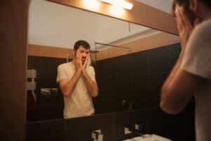Man in white t-shirt reflects in bathroom mirror