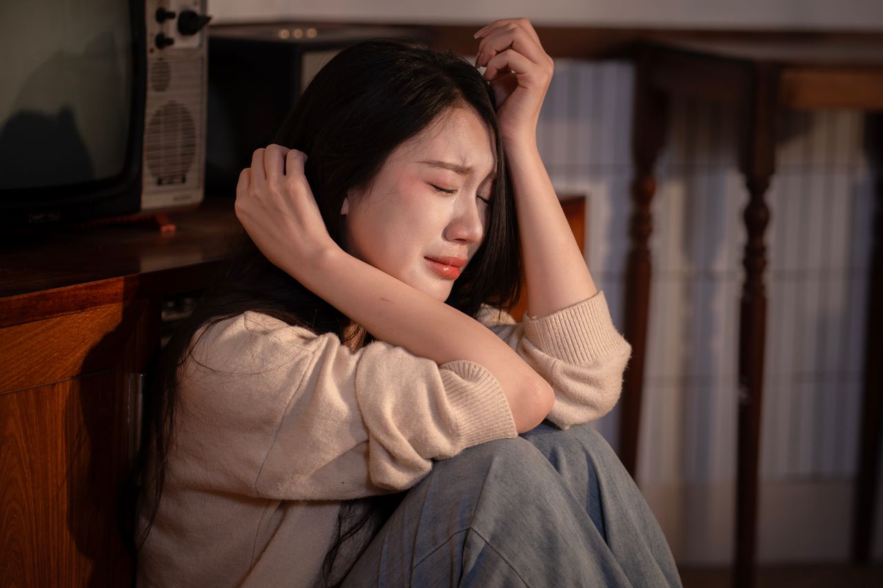 A young woman sitting indoors, expressing deep emotional distress
