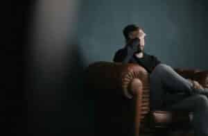 man holds his head while sitting on a sofa