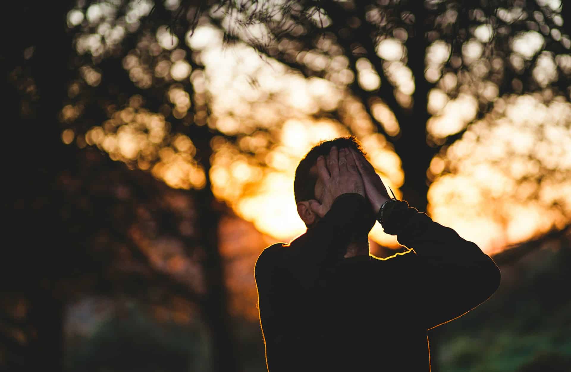 man wearing black long-sleeved shirt covering his face with hands