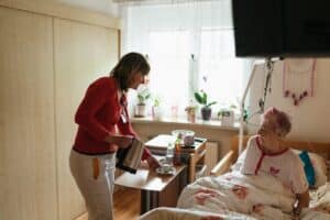 caregiver serves tea to a senior woman in a cozy bedroom setting
