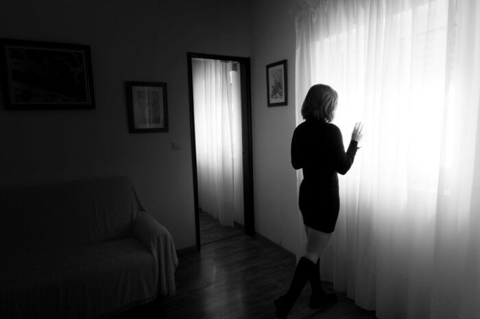 A woman stands by a window with curtains