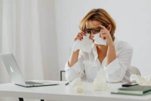 A woman in glasses is wiping tears while seated at a desk