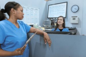 Nurses in scrub suits discussing medical tasks in a clinical environment