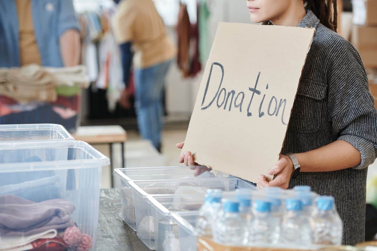A volunteer holds a cardboard donation sign at a charity event with donation boxes ready for collection