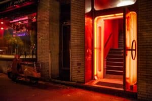 Illuminated entrance of a nightclub with neon red lights and a vintage scooter