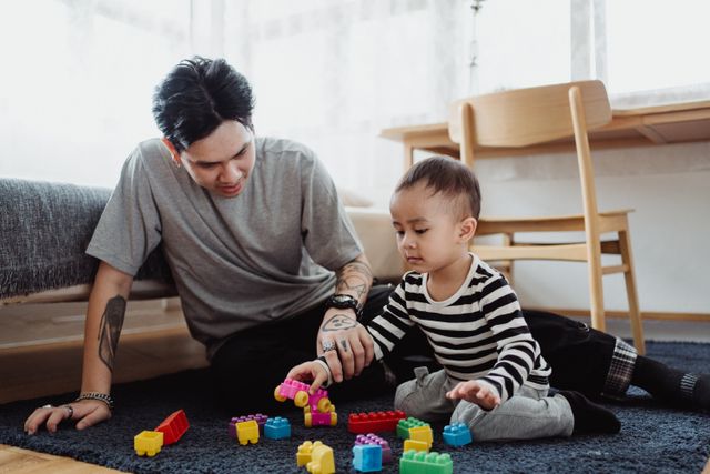 father playing blocks with his young child on the floor