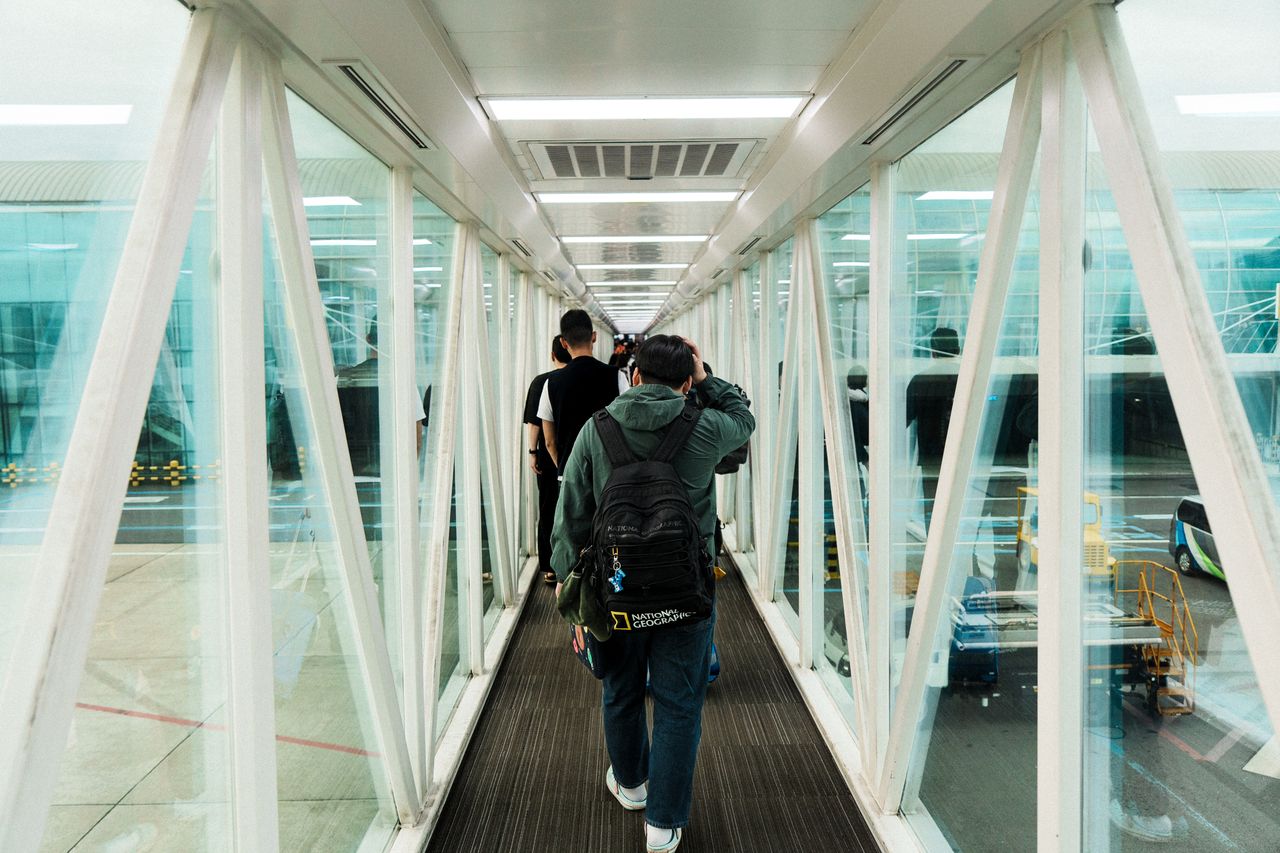 Travelers moving through a modern glass jet bridge at an airport