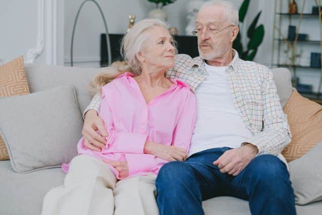 A senior couple lovingly embraces while sitting on a cozy sofa